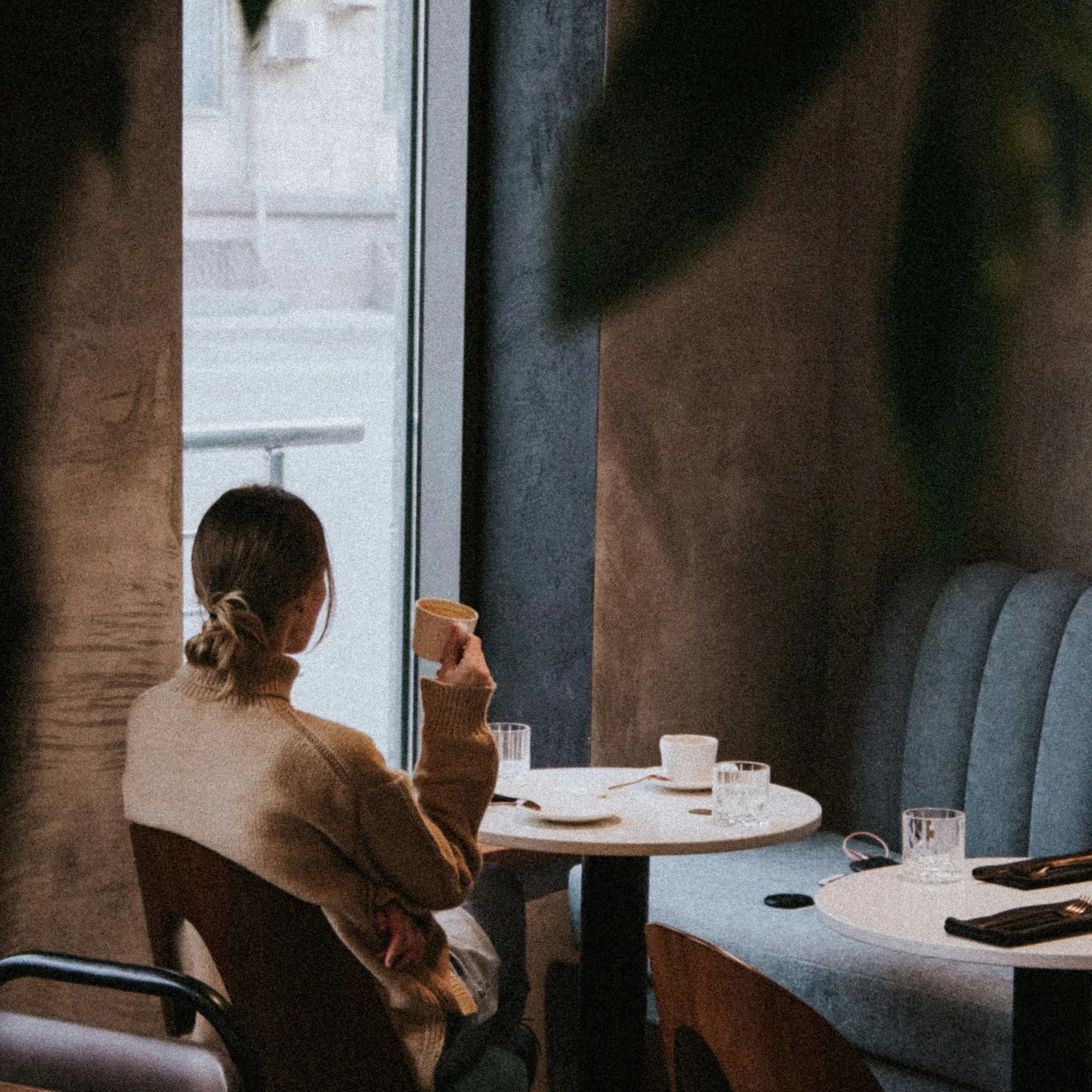 Woman seen from behind at a café table in warm window light