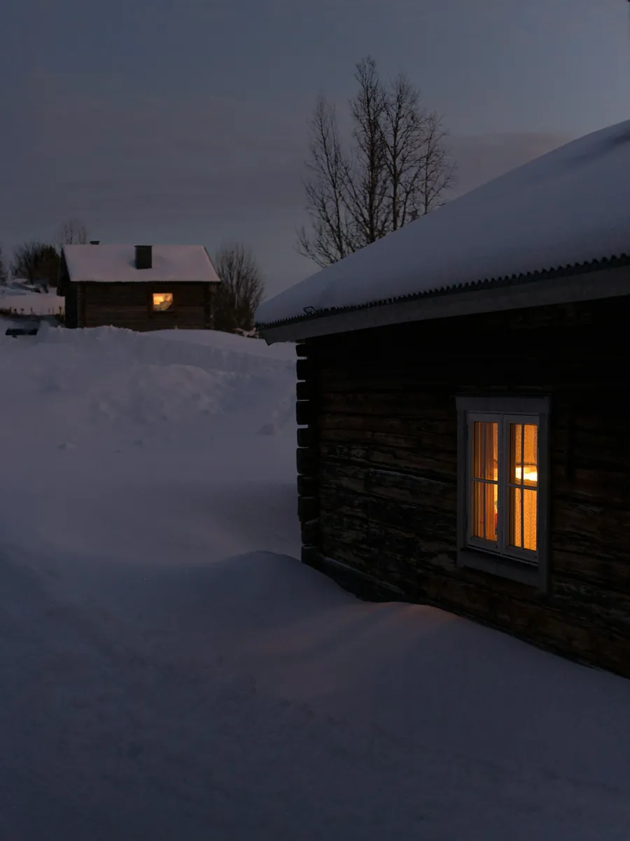 Small log cabin in the snow with a lit window on a winter evening